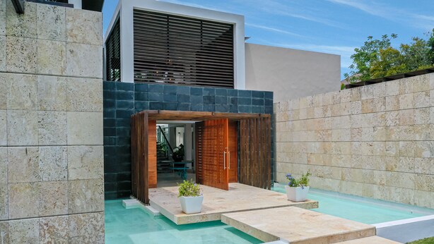 A modern outdoor pool area with stone walls, a wooden entrance, and potted plants. - Luxury villa at Puntacana Resort & Club (Punta Cana)