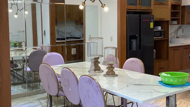 A modern kitchen with wooden cabinets, a marble countertop, and a dining area with a white table and purple chairs. - Verdana Villa. (San Francisco de Macorís)