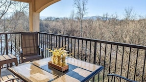 Ein Balkon mit Tisch und Stühlen, eine Vase mit Trockenblumen und Blick auf eine karge Landschaft mit Bäumen und Bergen.