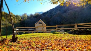 A wooden cabin with a gabled roof, surrounded by a wooden fence, set in a grassy field with autumn leaves. - Cab'ânes du Pibeste (Segus)