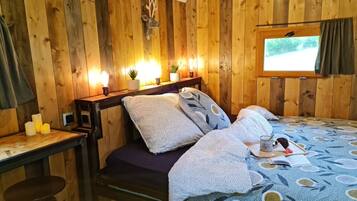 Un dormitorio acogedor de estilo cabaña con detalles de madera, una cama con ropa de cama estampada, un pequeño escritorio con una silla y una ventana con vistas al exterior.