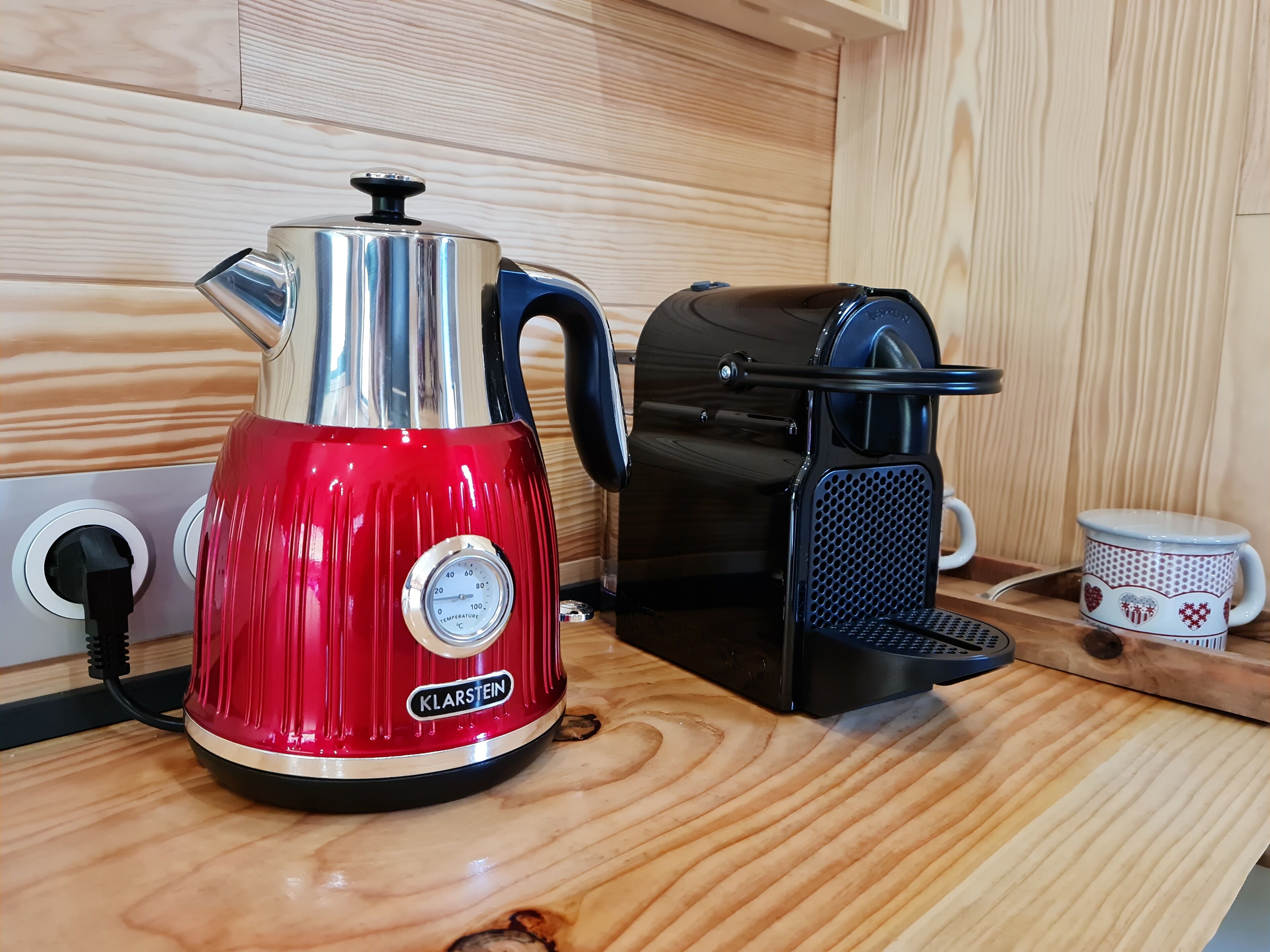 Eine rote Kaffeemaschine mit Temperaturanzeige und eine schwarze Espressomaschine auf einer Holzauskład.