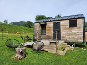 A rustic cabin with a wooden exterior, a black door, and a small porch with outdoor seating. - Cab'ânes du Pibeste (Segus)