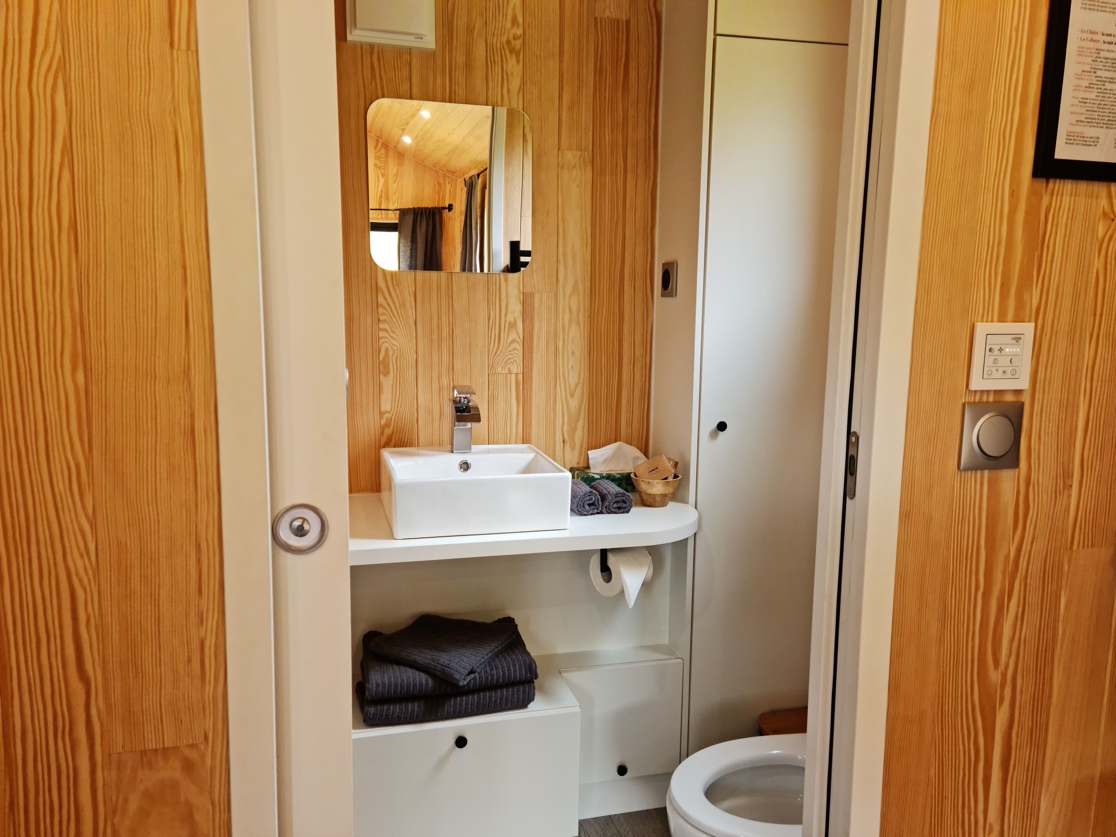 A compact bathroom with a wooden vanity, a sink, a toilet, and a mirror.
