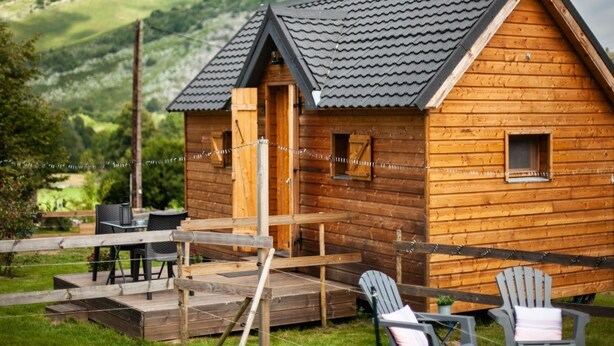 A wooden cabin with a pitched roof, a deck, and two Adirondack chairs. - Cab'ânes du Pibeste (Segus)