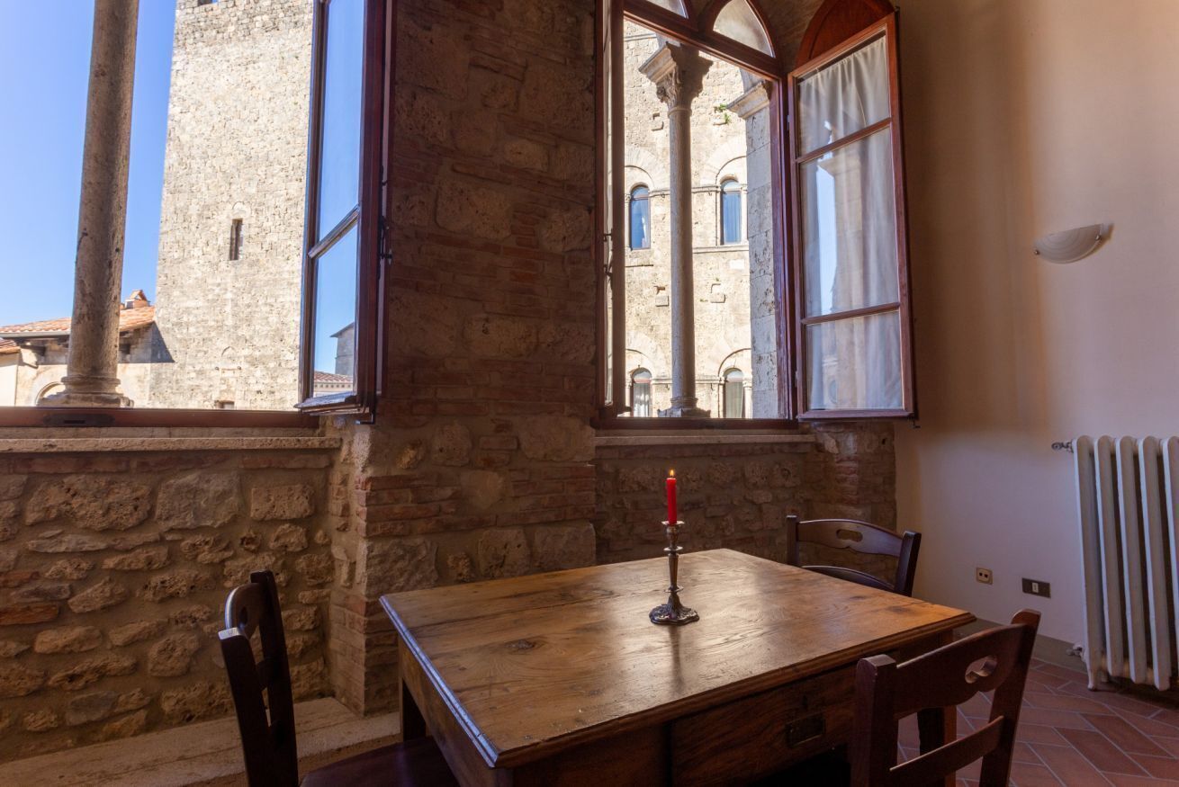 A rustic room with a wooden table and chairs, a window with curtains, and a stone wall.