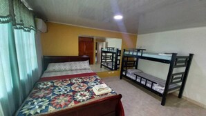 Una habitación con una cama individual, una litera, cabecera de madera, colcha y una ventana con cortinas.