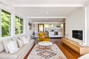 Una sala de estar moderna con un sofá, un sillón amarillo, una mesa redonda de centro y un televisor montado en la pared.
