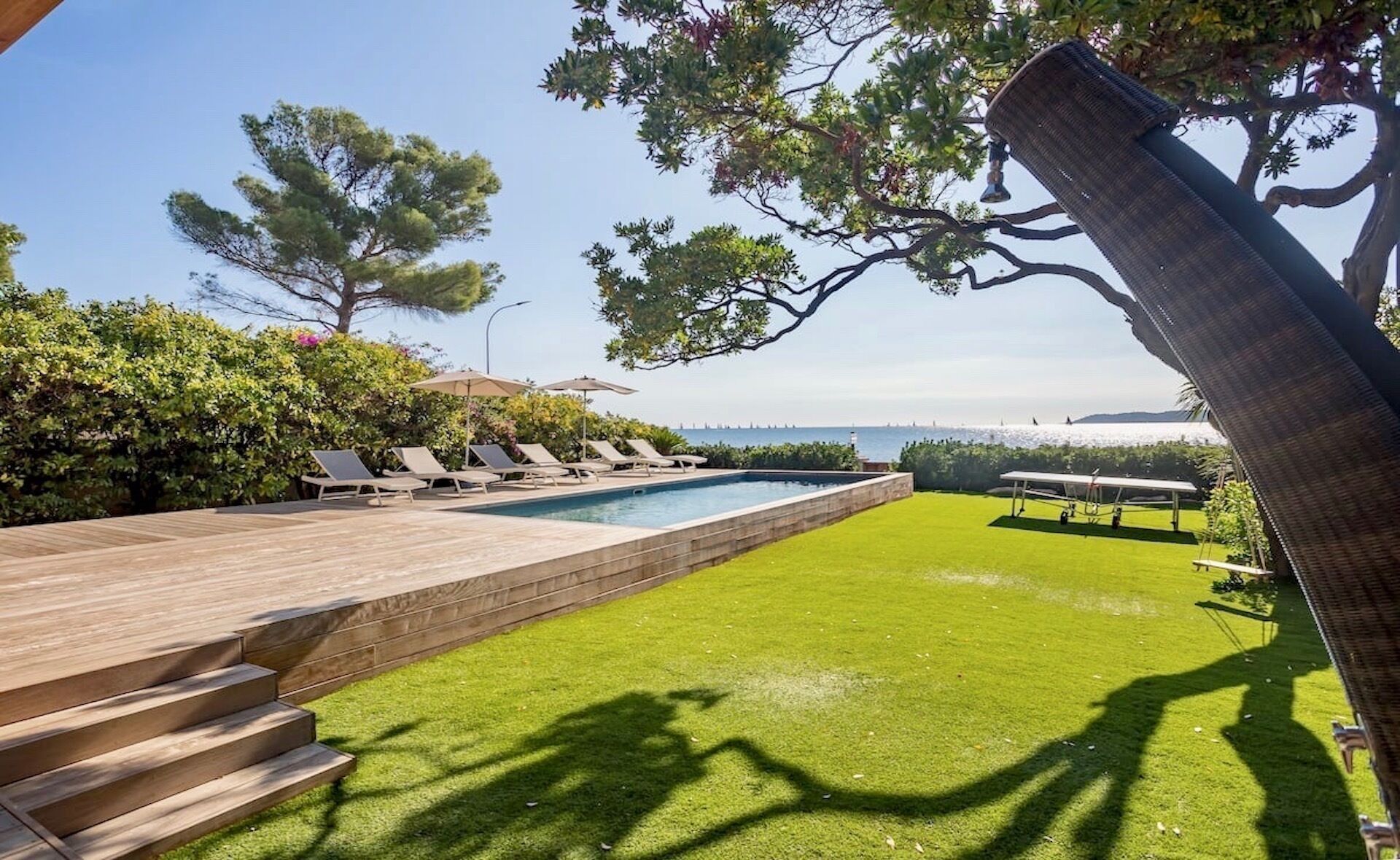 Un área de piscina con cubierta de madera, sillas de descanso y vista al mar.