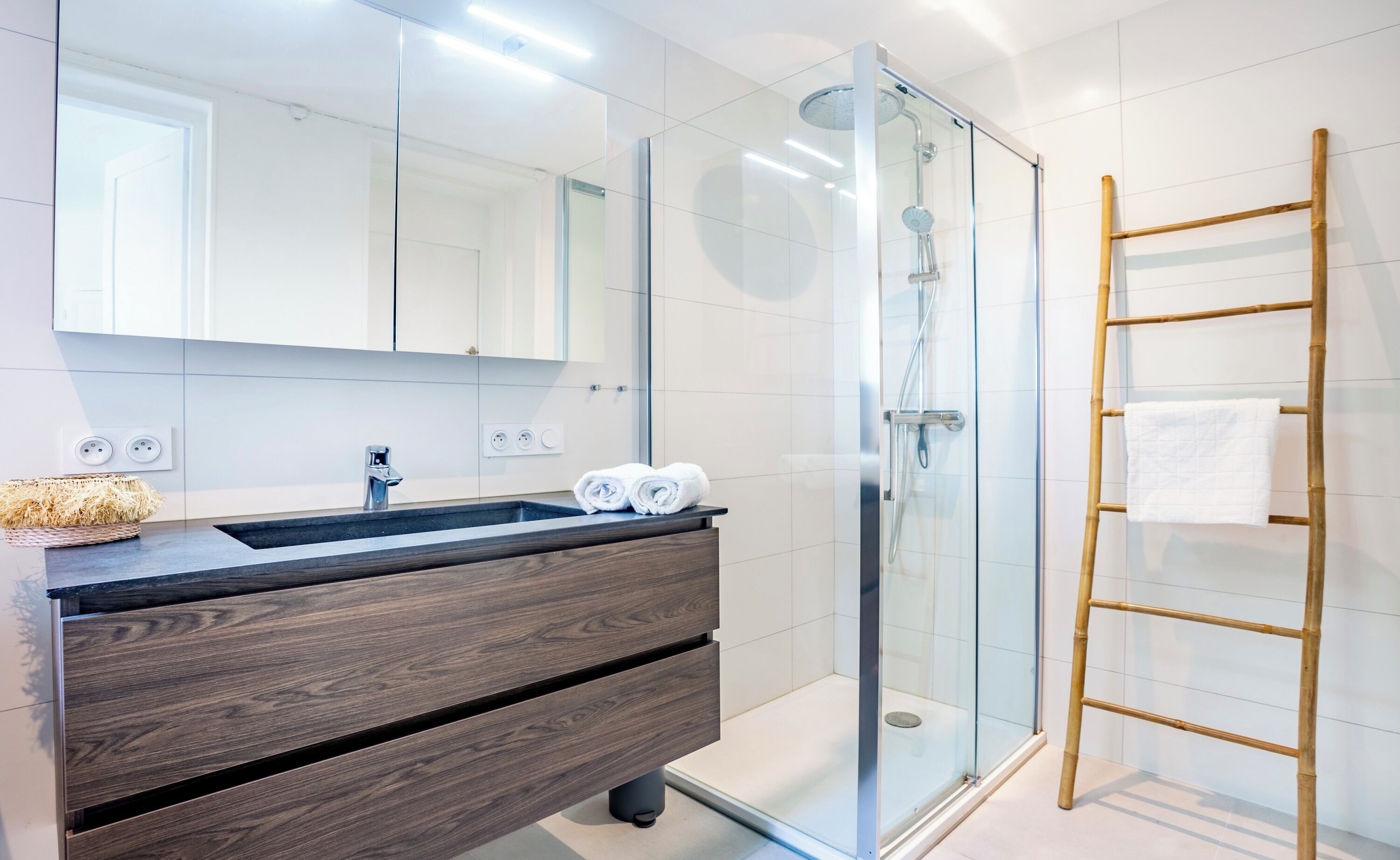 A modern bathroom with a glass shower enclosure, a wooden vanity with a sink, and a towel rack.