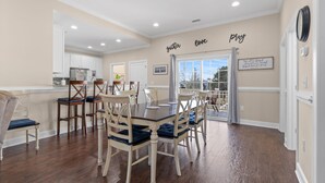 Un comedor con mesa y sillas de madera, una cocina al fondo y vistas a través de un ventanal.