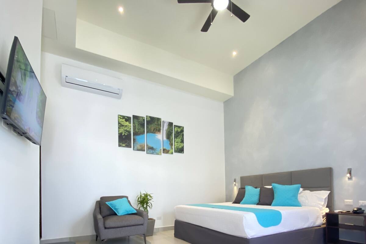 Un dormitorio moderno con una cama grande, un ventilador de techo y un televisor montado en la pared.