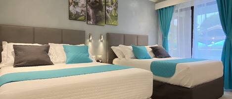 Habitación de hotel con dos camas, un ventilador de techo y un ventanal grande con cortinas.