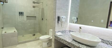 A modern bathroom with a glass-enclosed shower, a white toilet, a marble sink, and a large mirror.