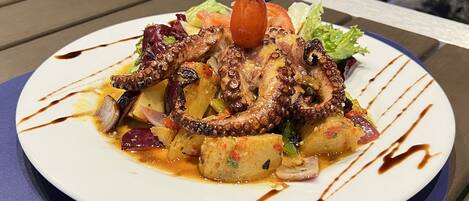 Un plato de comida con pulpo y verduras, servido en un plato blanco con un borde azul.