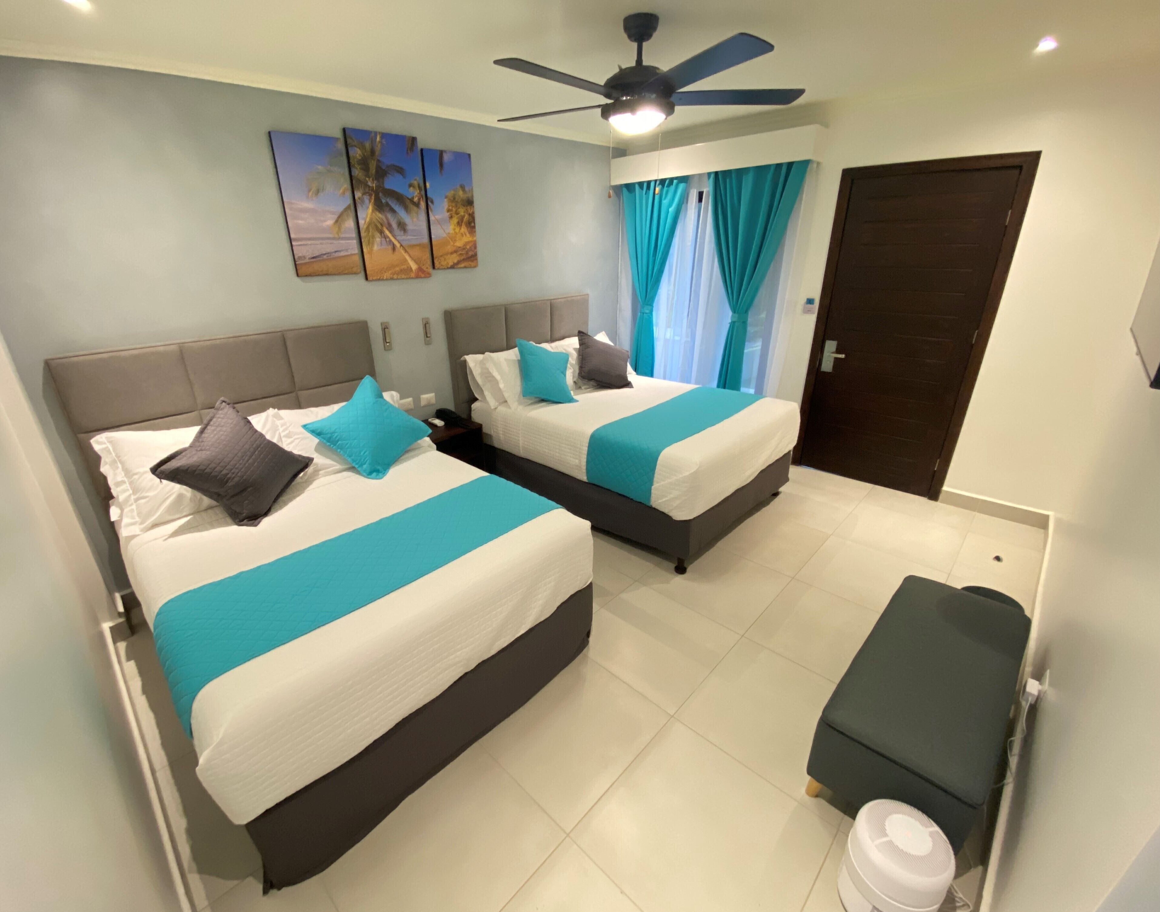 A hotel room with two beds, a ceiling fan, a small table, and a door.