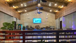 A spacious bar area with a high ceiling, wooden beams, and pendant lighting. A television is mounted on the wall, and there are various bar amenities visible. - Hotel Naoz (Quepos)