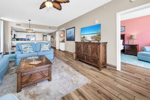 Un salon comprenant un canapé, une table basse, un meuble en bois et un tableau représentant une scène de plage.