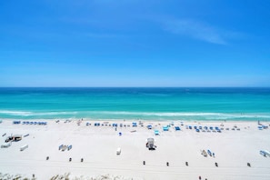 A beach with white sand, clear blue water, and blue umbrellas.