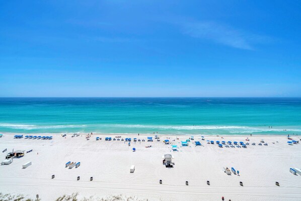Une plage de sable blanc, avec une eau d’un bleu limpide et des parasols bleus.