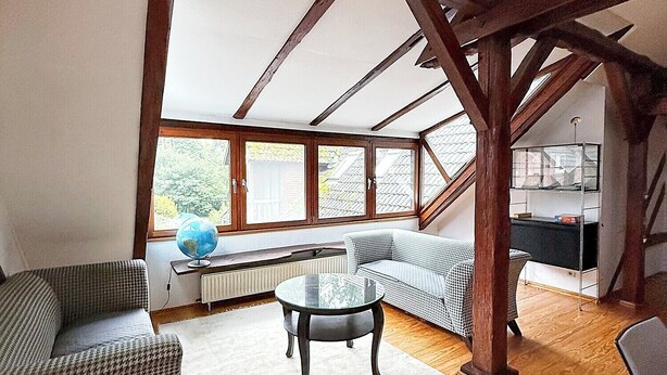 Une pièce mansardée spacieuse avec des poutres apparentes, une table en verre, un canapé et une vue sur l’extérieur.