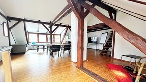 Un loft spacieux avec des poutres apparentes, un coin repas, un téléviseur et un escalier.