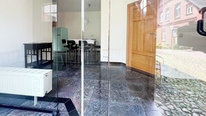 Une pièce avec une cloison en verre, un radiateur, une table avec des chaises et une porte en bois.