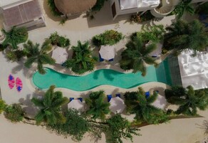 An aerial view of a resort with a swimming pool, lounge chairs, and palm trees.