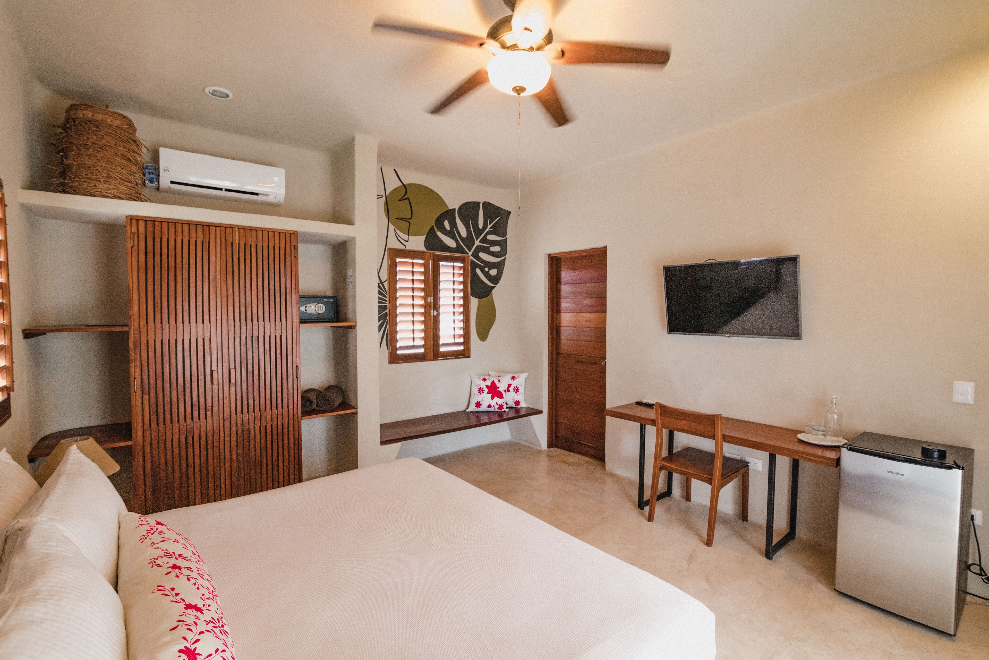 Un dormitorio con cama, escritorio, silla, armario, televisor y ventilador de techo.