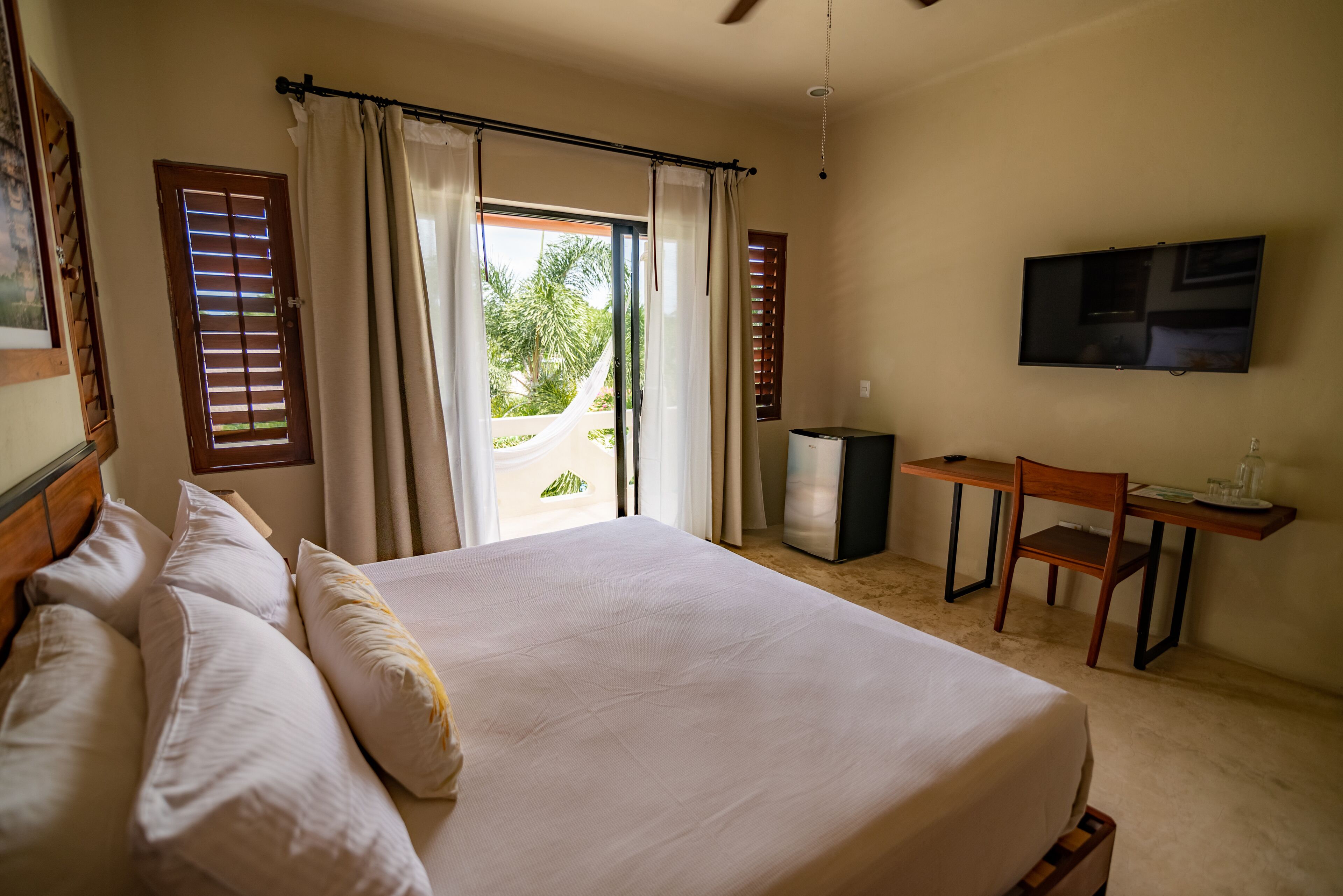 A bedroom with a bed, a desk, a chair, a television, and a view of the outdoors.