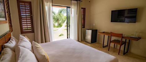 A bedroom with a bed, a desk, a chair, a television, and a view of the outdoors.
