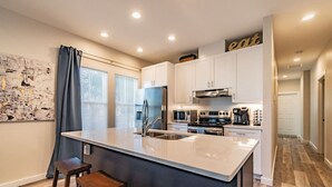 Une cuisine moderne avec des meubles blancs, un grand îlot central doté de tabourets, un réfrigérateur en acier inoxydable et un four à micro-ondes.