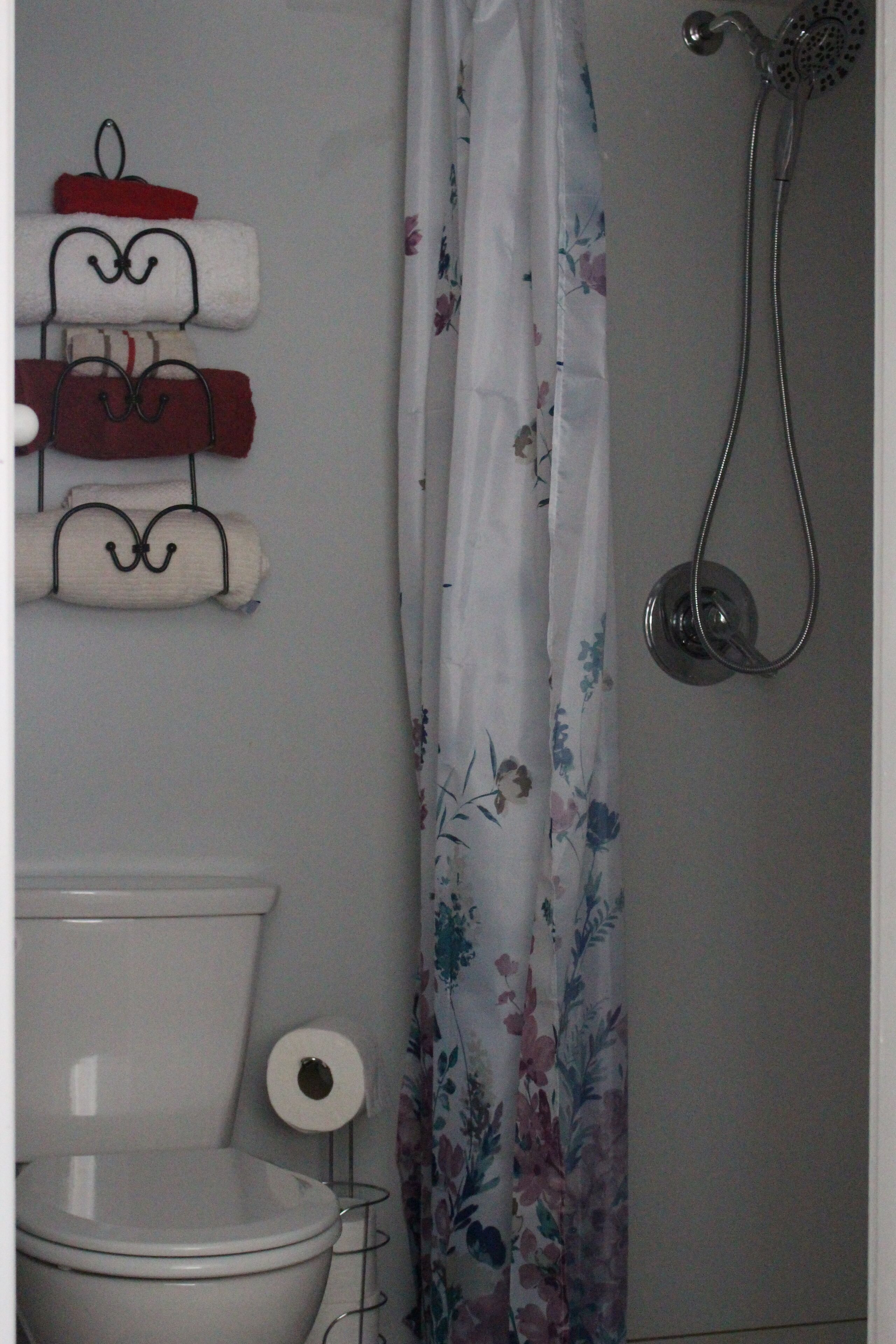 A bathroom with a toilet, a shower, and a towel rack with folded towels.