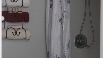 A bathroom with a toilet, a shower, and a towel rack with folded towels.