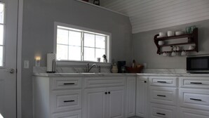 A kitchen with white cabinetry, a window, a microwave, and a coffee maker. - Little House in the Pine Woods (Heavener)