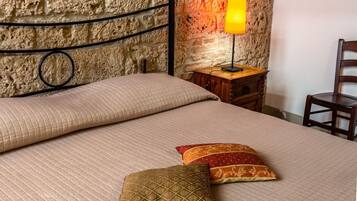 Una cama con cubierta acolchada, dos almohadas, una mesita de noche con lámpara y una silla de madera.