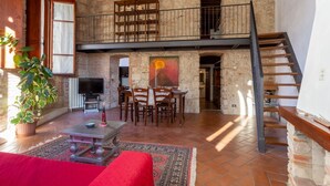 A spacious living area with a high ceiling, exposed brick walls, a wooden staircase, and a dining area with a table and chairs.