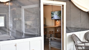 A room with a bed, a TV mounted on the wall, and a bar area with stools. - 15 Son's Geronimo - Birdhouse Cabin (Seguin)