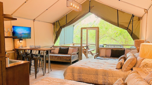 A tented accommodation with a dining area, a TV, and a bed with patterned bedding. - 15 Son's Geronimo - Birdhouse Cabin (Seguin)