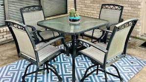 Un patio con una mesa de vidrio y cuatro sillas, una sombrilla y un cactus como centro de mesa.
