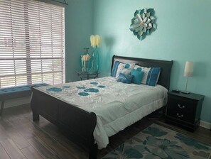 A bedroom with a bed, bedside table, lamp, and a wall decoration.