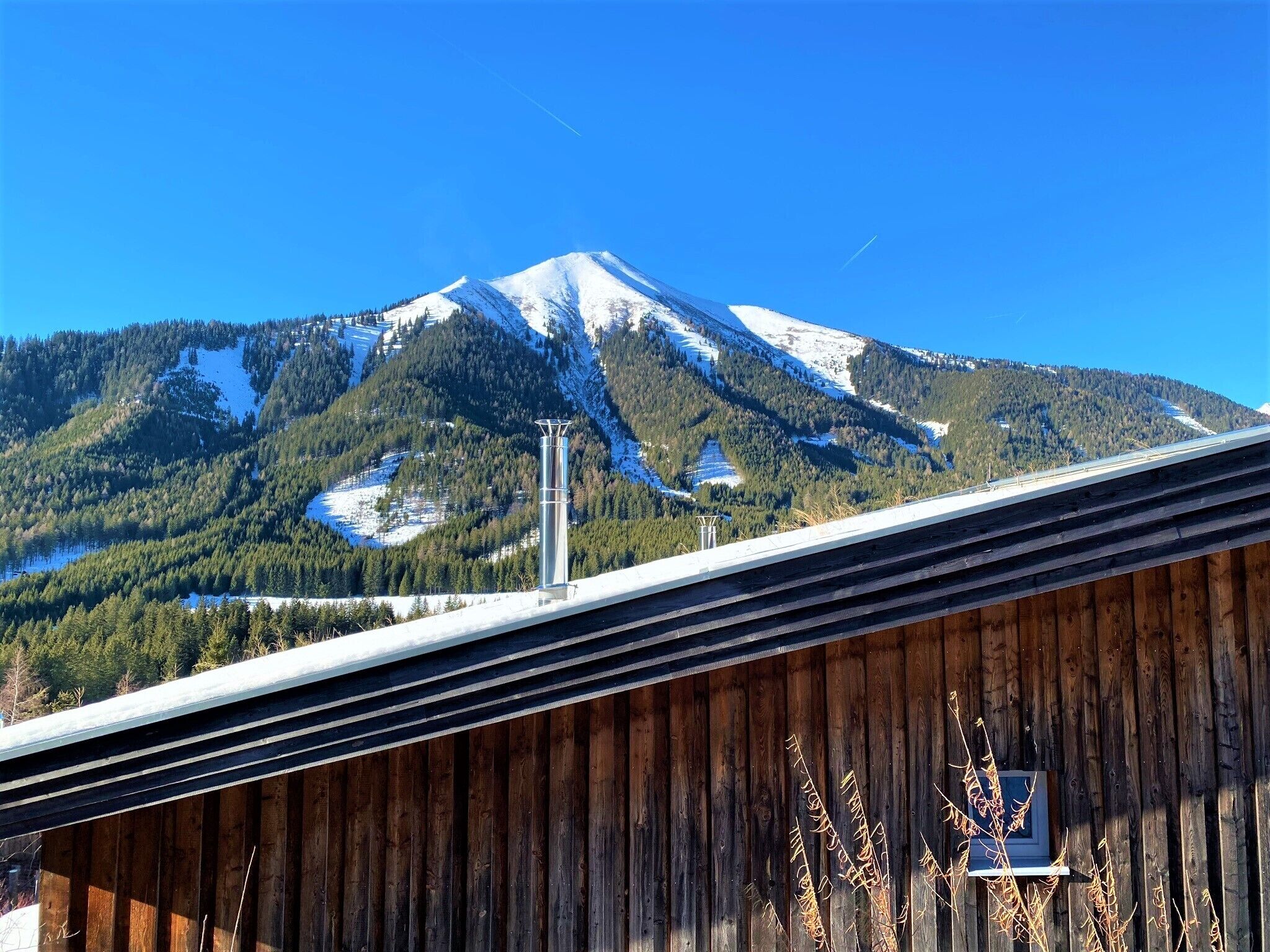 Une montagne aux sommets enneigés, une structure en bois au premier plan et un ciel bleu dégagé.