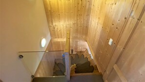 A wooden interior with a staircase, wooden walls, and a glass railing.
