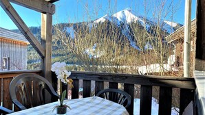 A wooden deck with a table and chairs, overlooking a snow-covered mountain.