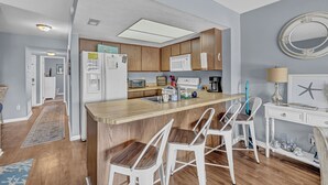 Een moderne keuken met houten kastjes, een centraal kookeiland met barkrukken, een magnetron en een koelkast.