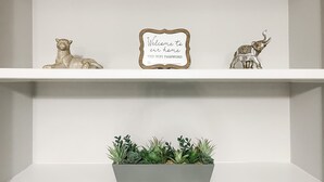 Une étagère blanche sur laquelle sont posés un cadre avec une inscription, une figurine de chat, une figurine de taureau et un pot de fleurs contenant des plantes vertes.