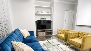 Un salon avec un canapé bleu, une table basse en verre et deux fauteuils jaunes.