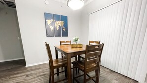 Un coin repas avec une table en bois et quatre chaises, une œuvre d’art représentant une carte du monde accrochée au mur, et une fenêtre avec des stores.