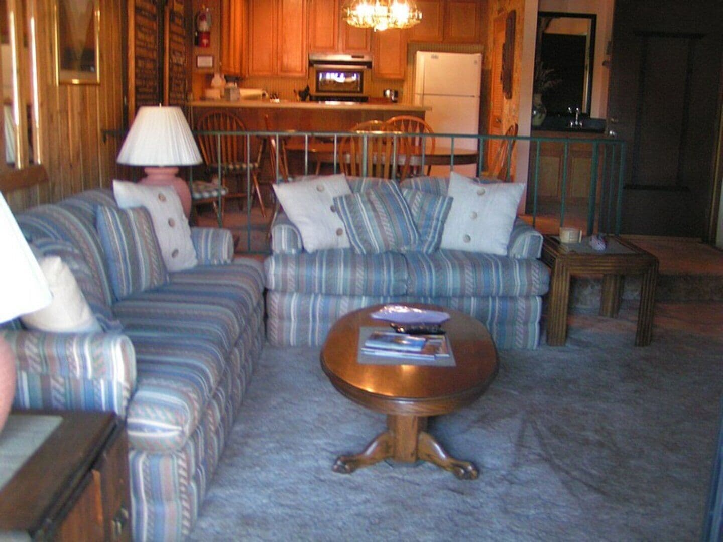 Una sala de estar con sofás a rayas, una mesa de centro de madera y una cocina al fondo.