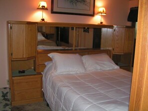 A bedroom with a bed, bedside tables, a mirror, and two wall-mounted lamps.